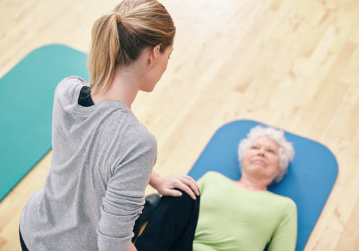 Female coach helping senior woman exercising in gym