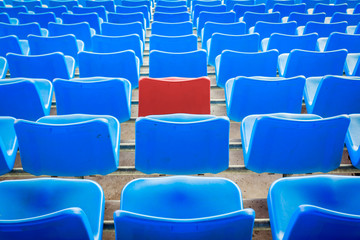 An empty red chair, arounded by blue chairs at the football Stad