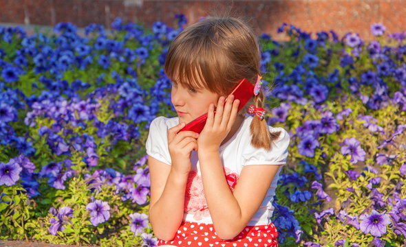 Little girl talking on cell phone on background of flowers