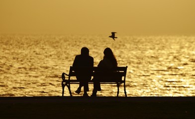 young couple sitting on a bench under sunset