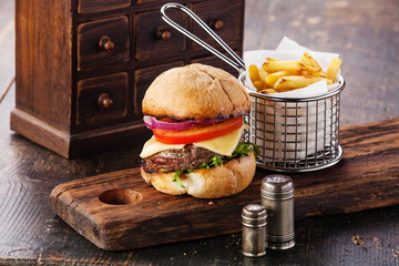 Burger with meat and French fries in basket on wooden background