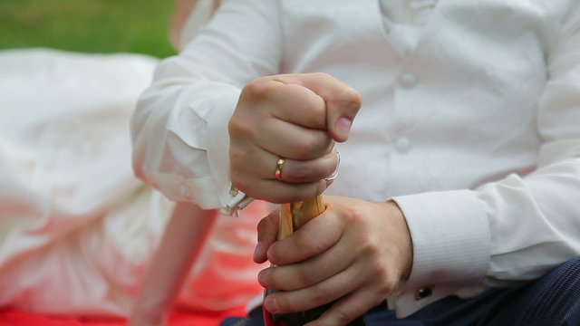 The groom opens a bottle of champagne at a wedding picnic