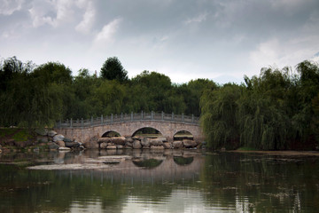 Fototapeta na wymiar Traditional Chinese stone bridge across the lake lost in green t