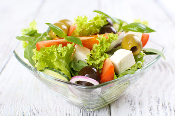 Greek salad in glass dish on color wooden table background