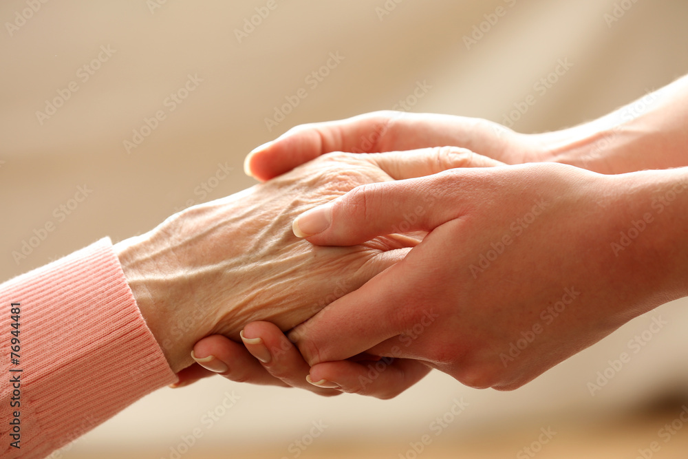 Wall mural Old and young holding hands on light background, closeup