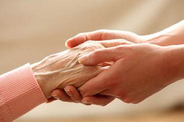 Old and young holding hands on light background, closeup