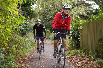 Two Mature Male Cyclists Riding Bikes Along Path