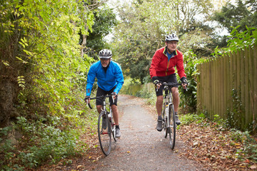 Fototapeta na wymiar Two Mature Male Cyclists Riding Bikes Along Path