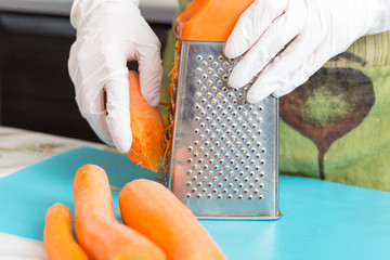Grate the carrots on grater in white disposable gloves