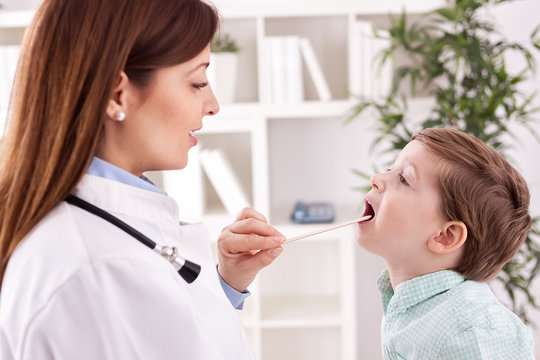 Smiling young doctor examining throat to child patient