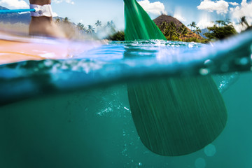 Oar of paddle boarder half way submerged in ocean water paddling