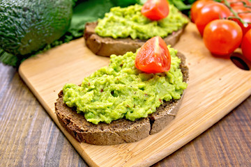 Sandwich with guacamole and tomatoes on dark board