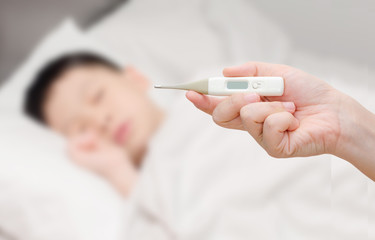 Mother holding digital thermometer and sick little boy in bed