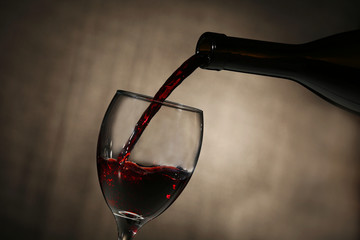 Naklejka na ściany i meble Pouring red wine from bottle into glass on dark background
