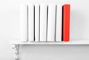 Blank books with red one on bookshelf on white wall background