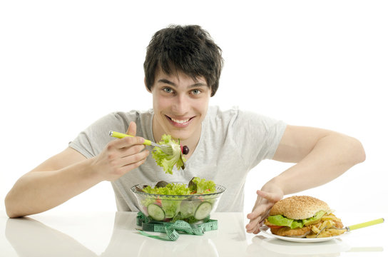Young man holding in front a bowl of salad and a big hamburger