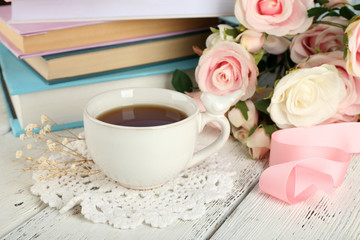 Cup of tea with books and flowers on wooden background