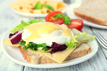 Toast with egg Benedict and tomato on plate on wooden table