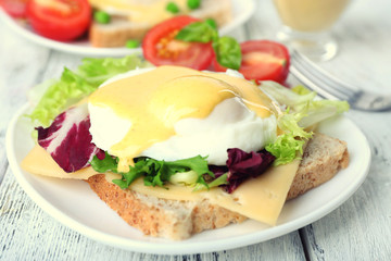 Toast with egg Benedict and tomato on plate on wooden table