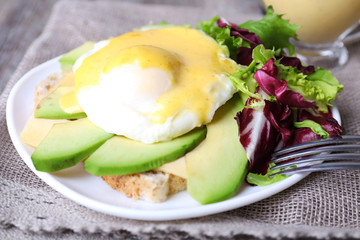 Toast with egg Benedict and avocado on plate on table close up