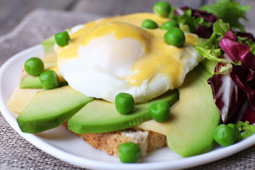 Toast with egg Benedict and avocado on plate on table close up