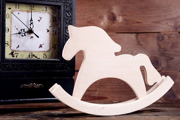 Retro clock with decorative horse on table on wooden background