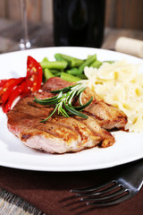 Steak with vegetables and pasta on plate on wooden plate