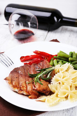 Steak with vegetables and pasta on plate on wooden plate