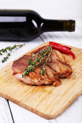 Steak with herbs on wooden stand and wine on table close up
