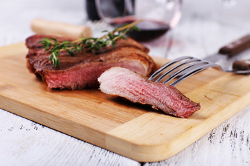 Steak with herbs on wooden stand and wine on table close up