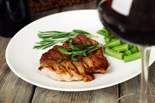 Glass of wine and steak with herbs on plate on wooden