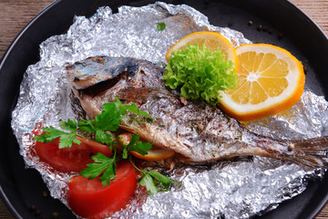 Tasty baked fish in foil on table close-up