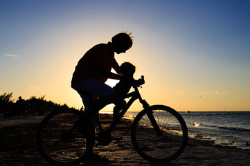 Silhouette of father and baby biking at sunset