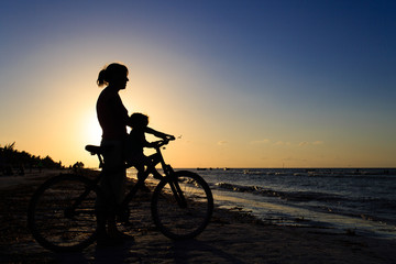 Fototapeta premium Silhouette of mother and baby biking at sunset