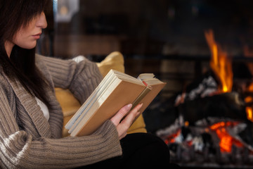 Woman reading a book by fireplace