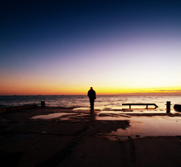 Man is standing on a jetty looking the sunset