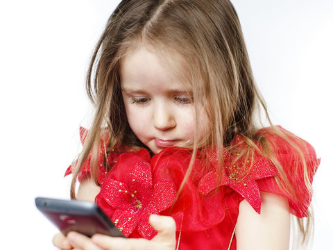 Cute little girl dressed in ball gown playing with smartphone