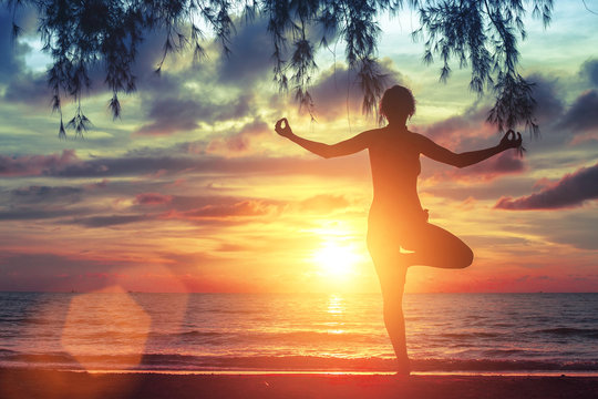 Yoga girl practicing on the ocean beach at amazing sunset.