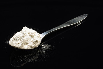Spoon of wheat flour isolated on the dark background