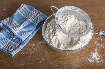 Sifted flour in a bowl on wooden background