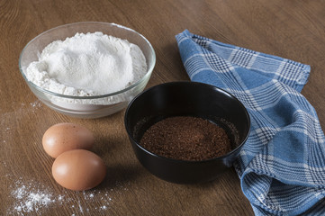 Flour in a bowl, eggs and brown sugar on wooden background