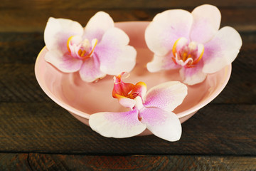 Fototapeta na wymiar Bowl with orchids on wooden background