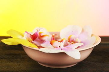 Fototapeta na wymiar Bowl with orchids on table on bright background