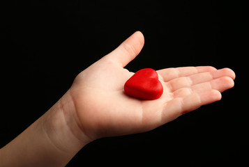 Heart in child hands on black background