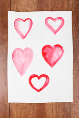 Painted hearts on sheet of paper on wooden table background