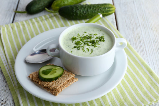 Cucumber soup in bowl on color wooden table background