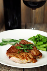 Steak with herbs on plate and bottle of wine on wooden table