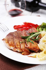 Steak with vegetables and pasta on plate on wooden plate