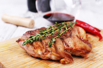 Steak with herbs on wooden stand and wine on table close up