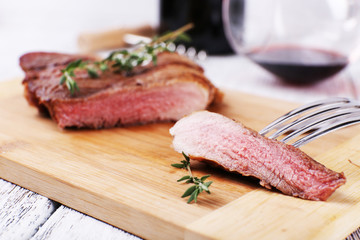 Steak with herbs on wooden stand and wine on table close up